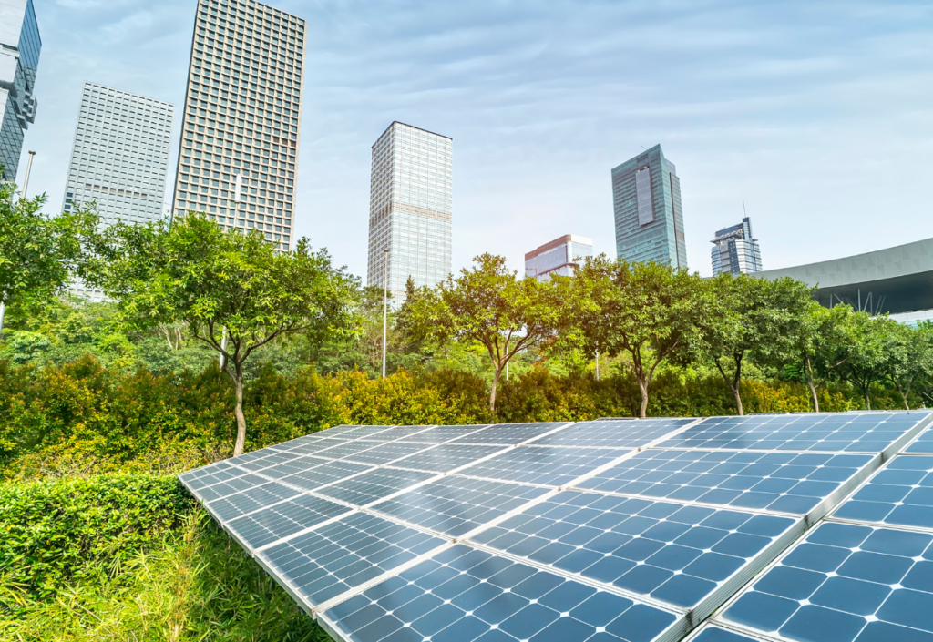 Solar panel in green field with cityscape in the background on a clear blue sky day.