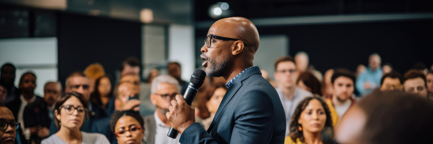 Person speaking into microphone in front of large crowd.