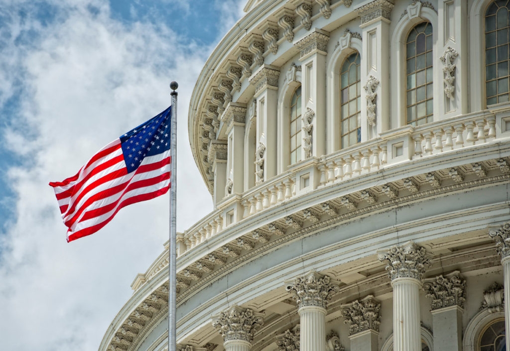 Capital building with American Flag on a pole with a blue sky and cloudy background.